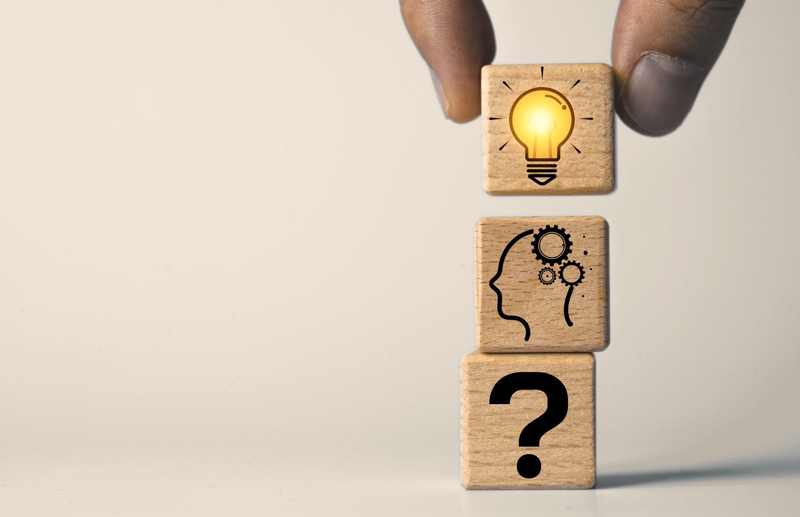 Three wooden blocks stacked: a question mark, a head with gears, and a glowing light bulb